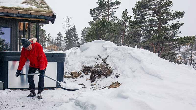 Mann som måker snø utenfor en hytte